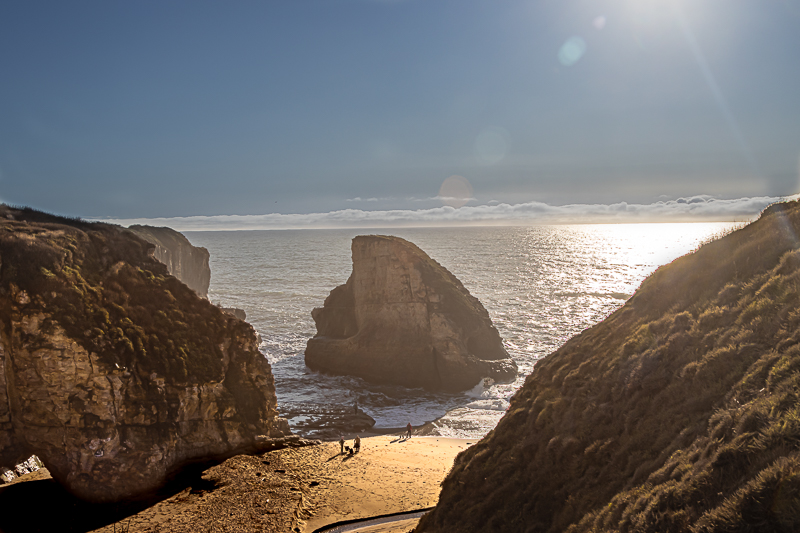Shark Fin Cove — natural cliffs frame a lone sea stack and sandy beach at golden hour